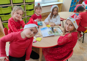 przedszkolaki siedzą przy stoliku w czerwonych ubraniach i czapkach