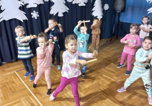 dzieci uderzają drewienkami o siebie z wyciągniętymi ramionami w prawą stronę