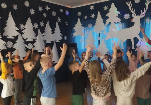 dzieci z panią Nutką stoją w kole, śpiewają i unoszą ręce w górę
