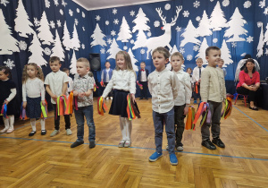 występy wnuków w czasie uroczystości babci i dziadka - dzieci stoją z kolorowymi wstążkami
