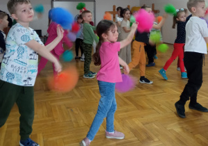 dzieci wymachują kolorowymi pomponami stojąc w szeregach