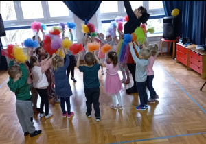 przedszkolaki stoją w gromadce obok pani Nutki z rękami uniesionymi w górę, w których trzymają kolorowe pompony