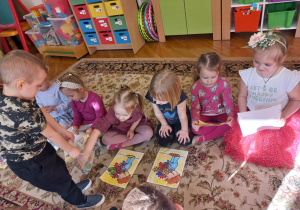 chłopiec częstuje dziewczynki siedzące na dywanie cukierkami