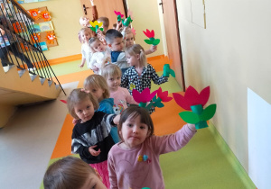 przedszkolaki idą przedszkolnym korytarzem i niosą kwiatki wykonane dla mam