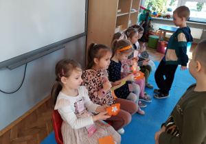 chłopcy składają życzenia dziewczynkom siedzącym na krzesełkach i wręczają im laurki