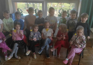 przedszkolaki pozują do zdjęcia grupowego w Dniu Kobiet a dziewczynki trzymają żółte żonkile