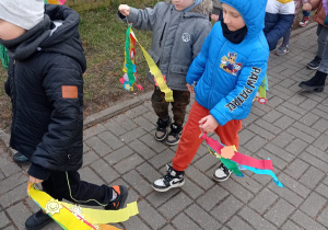 dzdzieci podczas spaceru po osiedlu z Marzannami niosą kolorowe wstążki