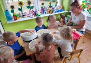 dzieci siedzą przy stoliku i układają jabłka na suszarkach, które kroi mama