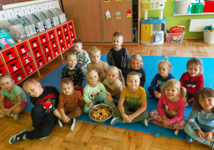 przedszkolaki siedzą w grupie na dywanie z miską pełną ususzonych jabłek