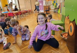 dziewczynka z zamkniętymi oczami odgaduje nazwę warzywa wyciągniętego z otworu drzewa za pomocą dotyku