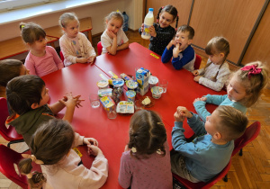 przedszkolaki siedzą przy stoliku wokół produktów mlecznych