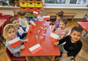 dzieci z wykonanymi przez siebie flagami wykonanymi z białych i czerwonych pasków papieru zamocowanych na patyczku
