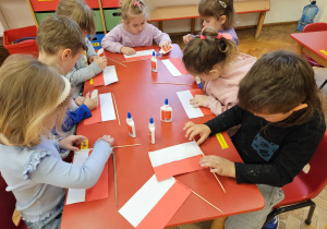 dzieci mocują patyczki do sklejonych pasków paieru tworzących flagę Polski