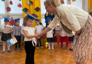 dziewczynka podczas pasowania na przedszkolaka ściska dłoń pani dyrektor