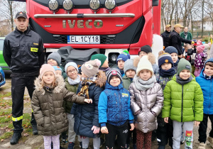 dzieci stoją przed wozem strażackim ze strażakiem