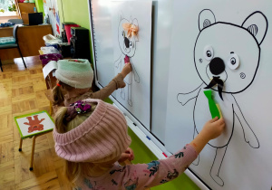 dziewczynki z zasłoniętymi oczami doklejają narysowanym misiom krawat czy uśmiech