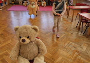 zabawa sprawnościowa - dziewczynka niesie na głowie misia i idzie slalomem między rozstawionymi po sali krzesełkami , na których siedzą misie