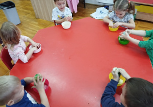 przedszkolaki ugniatają masę w miseczkach siedząc przy stoliku