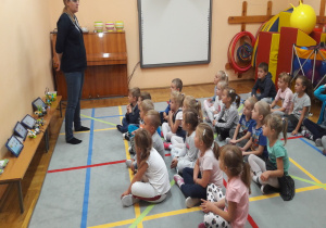 dzieci siedzą na macie i słuchają pani