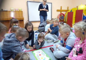 instruktorka stoi nad dziećmi a dzieci patrzą na poruszające się po drodze zaprogramowanego robota