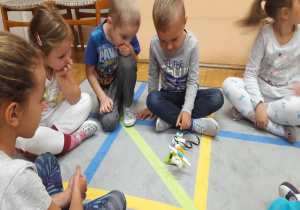 dzieci siedzą w kole a chłopiec bawi się robotem z klocków