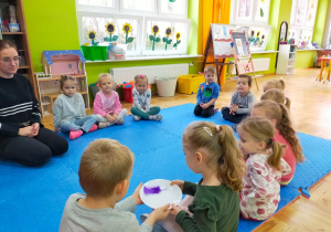 dzieci siedzą w kole i przekazują sobie kolejno talerzyk z piórkiem