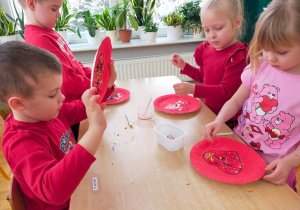 dzieci obsypują narysowane serca brokatem