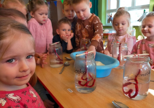 przedszkolaki robią doświadczenie ze słoną wodą i czerwonymi sznurkami w kształcie serduszek