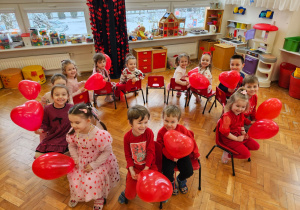 dzieci siedzą z czerwonymi balonami na krzesełkach ustawionych w kole