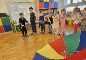 dzieci celują piłeczkami do dużego parasola