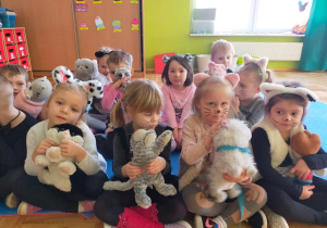 przedszkolaki siedzą z maskotkami kotków