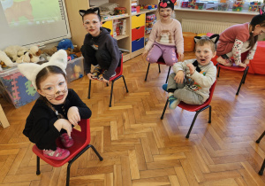 przedszkolaki w strojach kotów siedzą na krzesełkach i miauczą