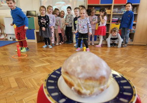 zabawa sprawnościowa - przedszkolaki skaczą do pączka z nogami włożonymi w kółko
