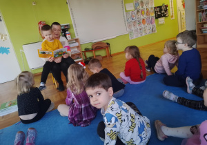 mama trzyma na kolanach syna i czyta pozostałym dzieciom bajkę