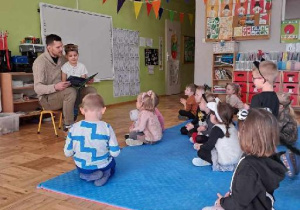 tata trzyma na kolanach córkę i czyta dzieciom bajkę