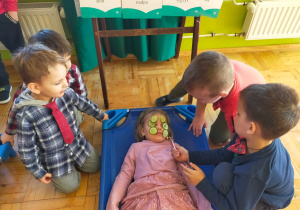 chłopcy masują twarz dziewczynki, która leży na leżaku