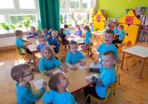 dzieci w niebieskich koszulkach kolorują motylki