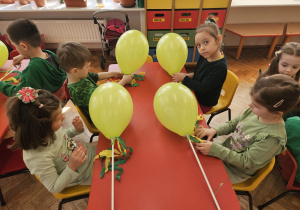dzieci przygotowują gaiki z zielonych balonów i mocują do patyków kolorowe paski bibuły