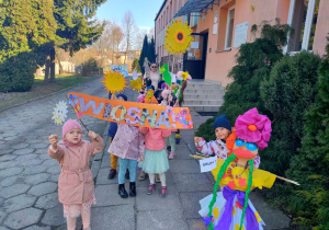 dzieci przed budynkiem przedszkola z Marzanną i banerem "wiosna"