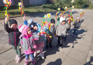 przedszkolaki ustawione w korowodzie przed budynkiem przedszkola z kwiatkami