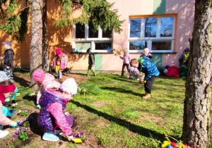 dzieci przed budynkiem przedszkola dosypują ziemi pod bratkami