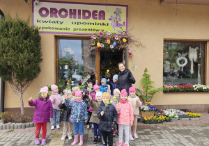 zdjęcie grupowe z nauczycielką przed kwiaciarnią z kwiatkami