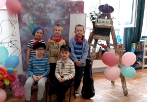 przedszkolaki w strojach artystów pozują do zdjęcia na tle płótna i obrazów