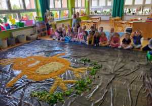 przedszkolaki siedzą przed rysunkiem usypanego z chrupek kurczaka