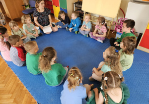dzieci siedzą w kole i słuchają bajki czytanej przez prowadzącą spotkanie