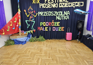 dekoracja festiwalowa - Tańcząca i śpiewająca Nutka między kolorową łódką , różową walizką a balonowym samolotem
