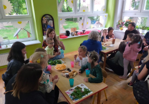 przedszkolaki z rodzicami siedzą przy stolikach i częstują się ziołowymi herbatkami