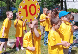 przedszkolaki w żółtych koszulkach stoją z tabliczką z zapisanym numerem 10