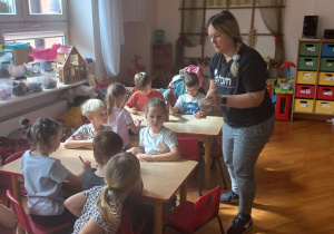 mama rozdaje arteczki dzieciom siedzącym przy stolikach