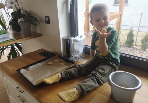 dziecko trzyma kulkę ciasta siedząc na blacie kuchennym pod oknem